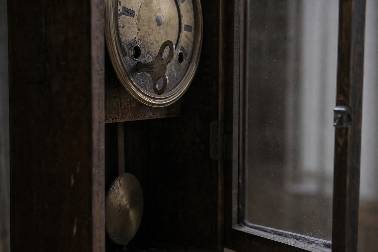 An old wall clock with its glass door open, a metal winding key set into the worn brass face.